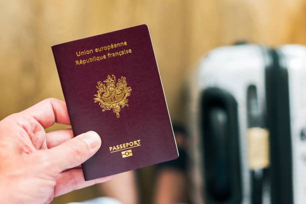 hand holding a french european passport with luggage in the background